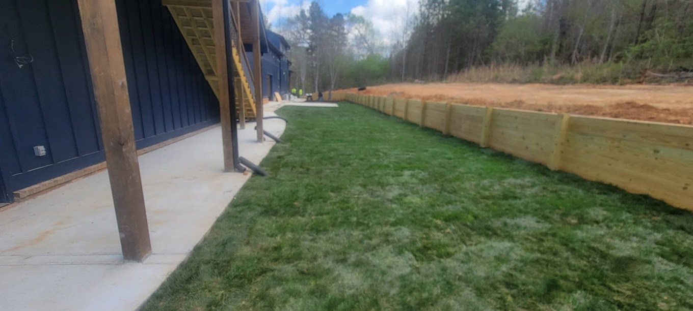 Finished timber retaining wall with fresh sod lawn and concrete walkway